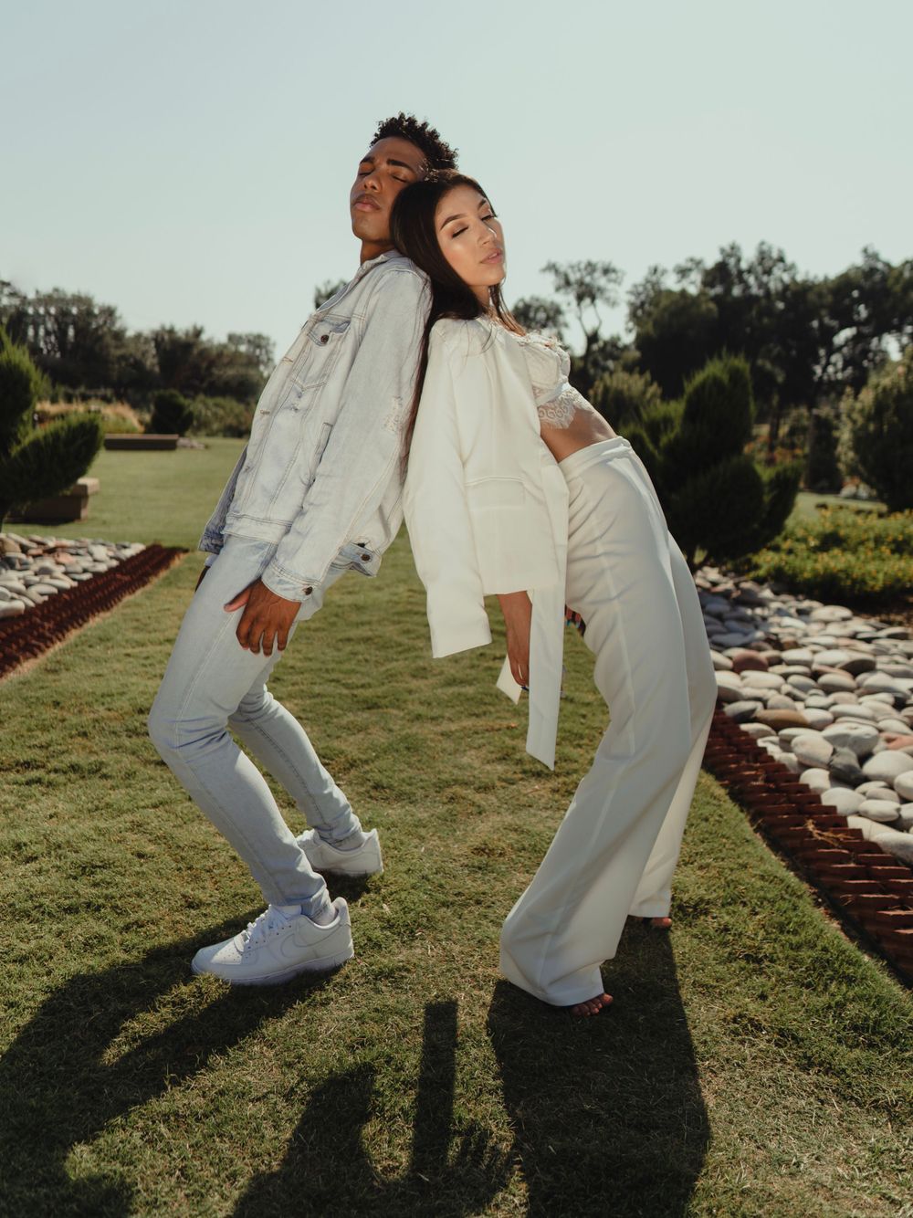 Models in all-white ensembles lean against each other in artistic outdoor pose.