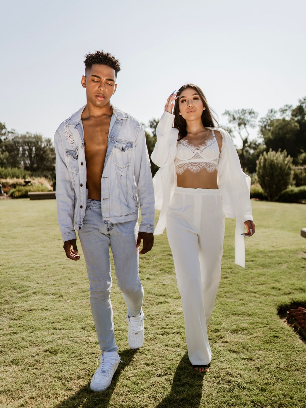 Models showcase contrasting denim and white outfits in sunny garden setting.