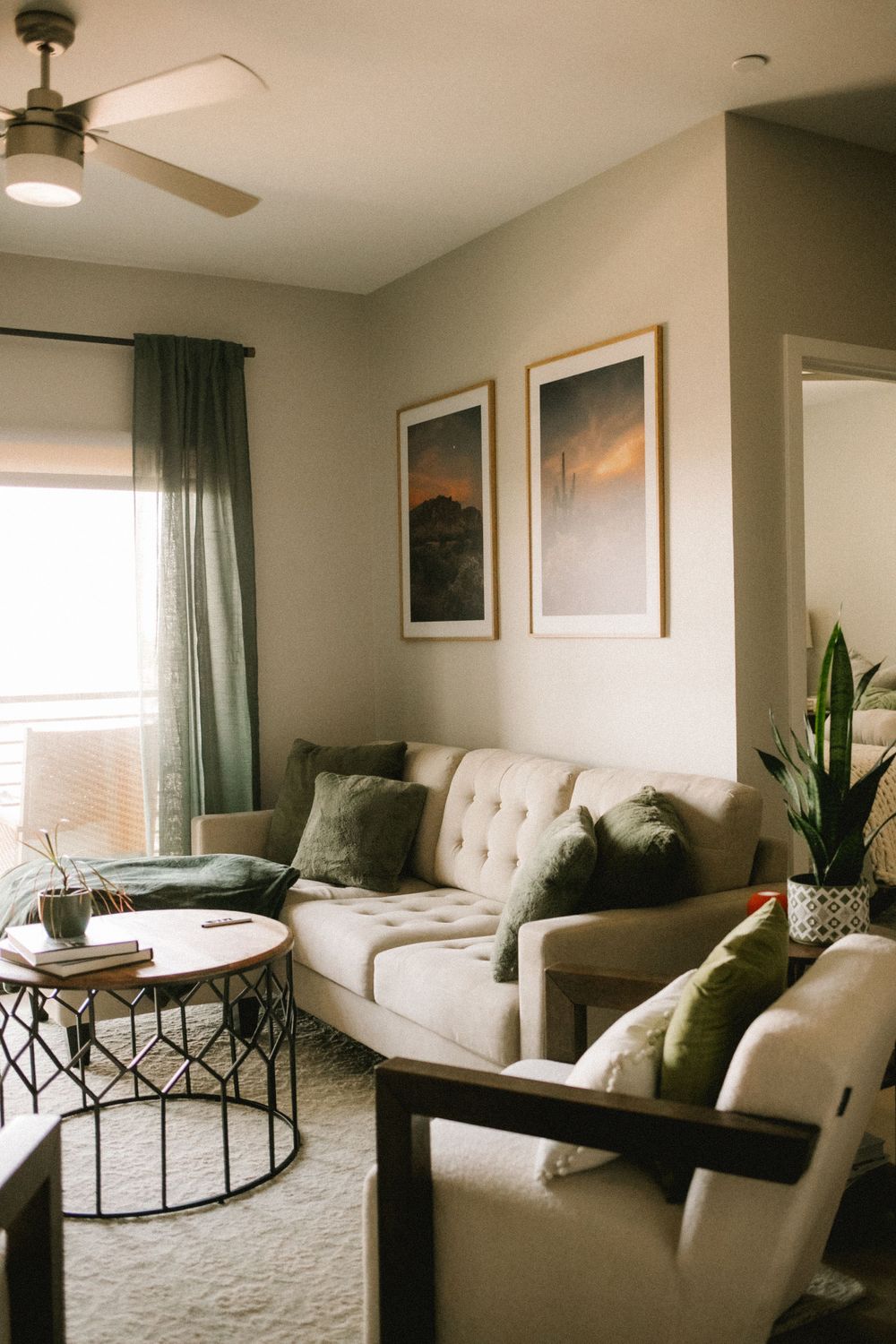 Cozy living room with tufted sofa, green pillows, desert artwork, and ceiling fan.
