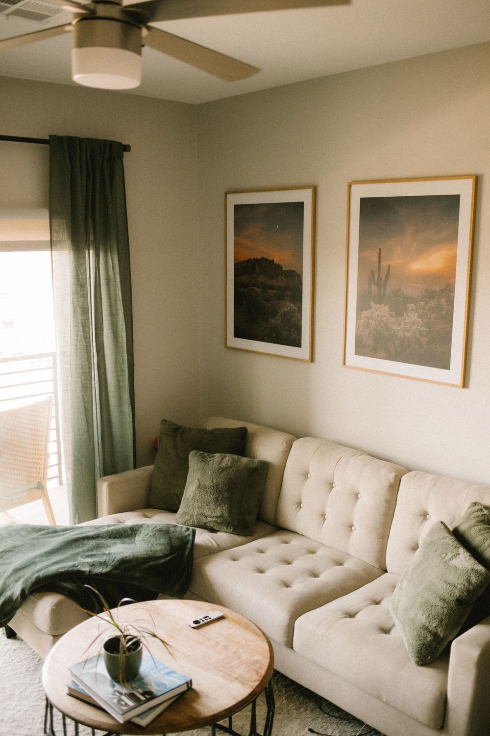 Neutral living room featuring tufted sofa, green throw, desert landscape framed prints, and ceiling fan.