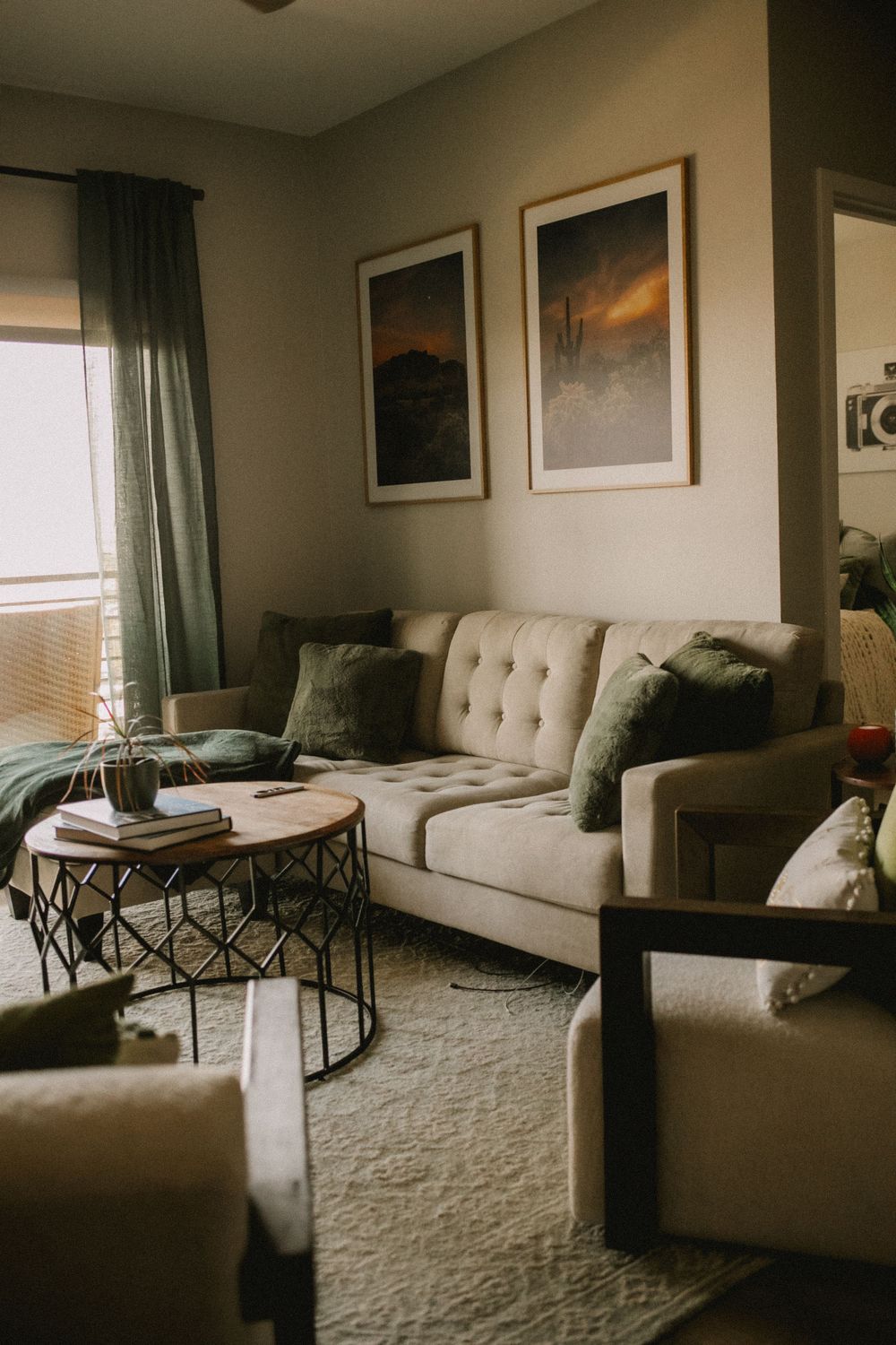 Modern living room with white tufted sofa, green accent pillows, round wood coffee table, and desert landscape wall art.