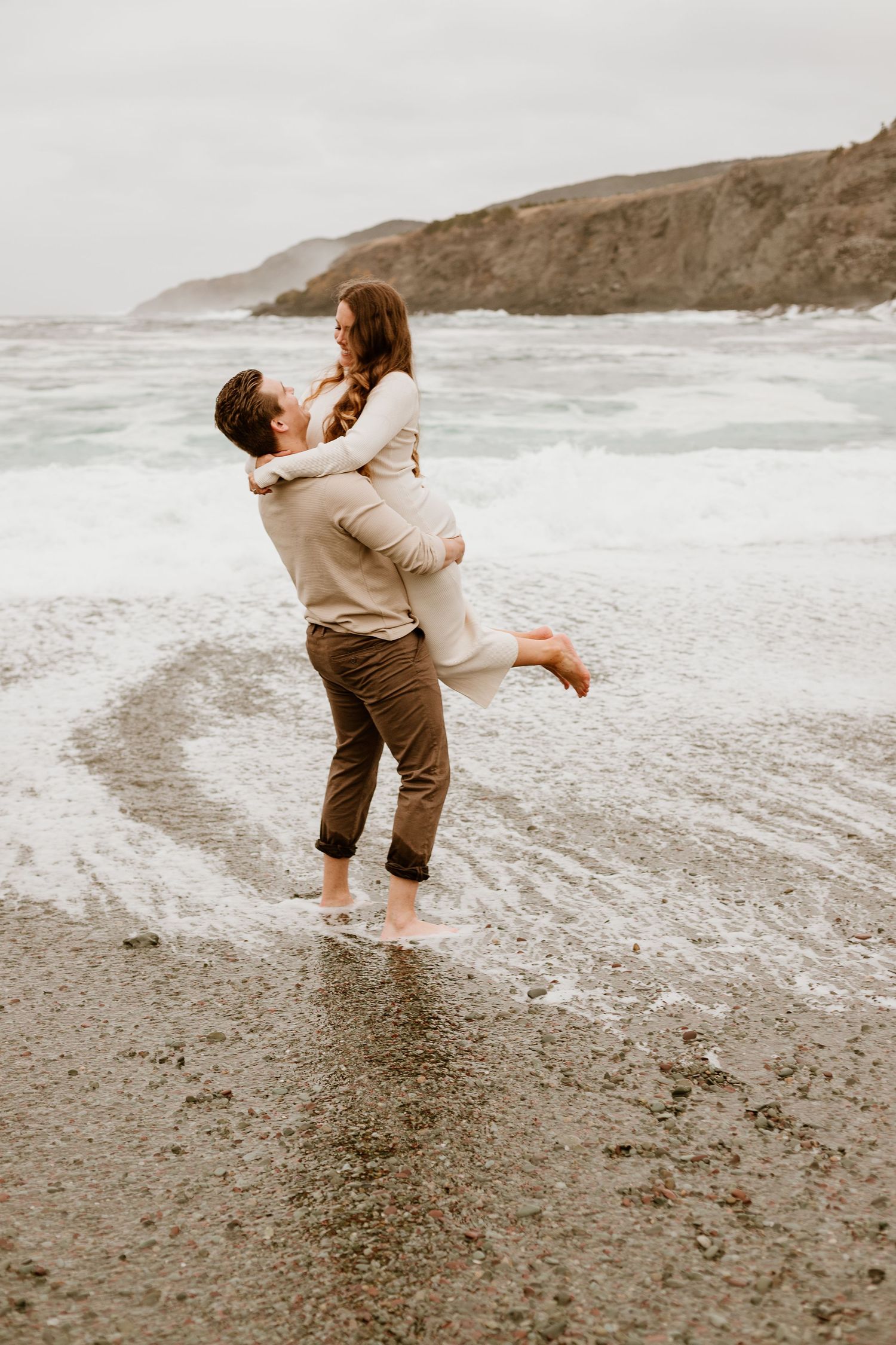 Man lifting his fiance up, with his feet in the Newfoundland beach water