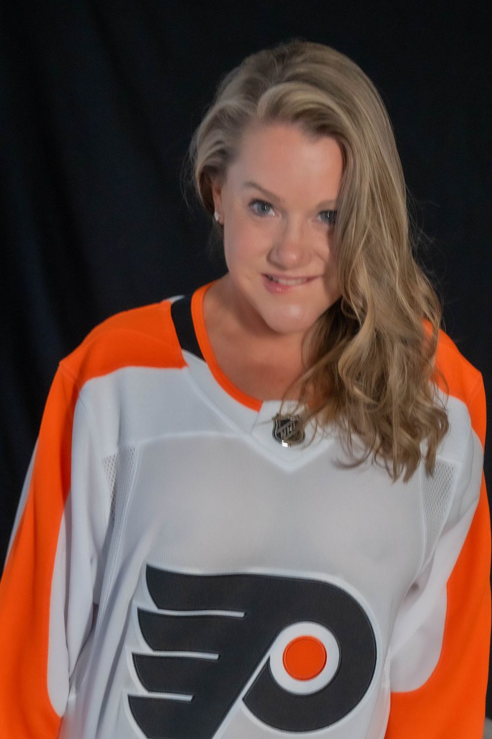 Woman wearing Philadelphia Flyers NHL hockey jersey against dark background.