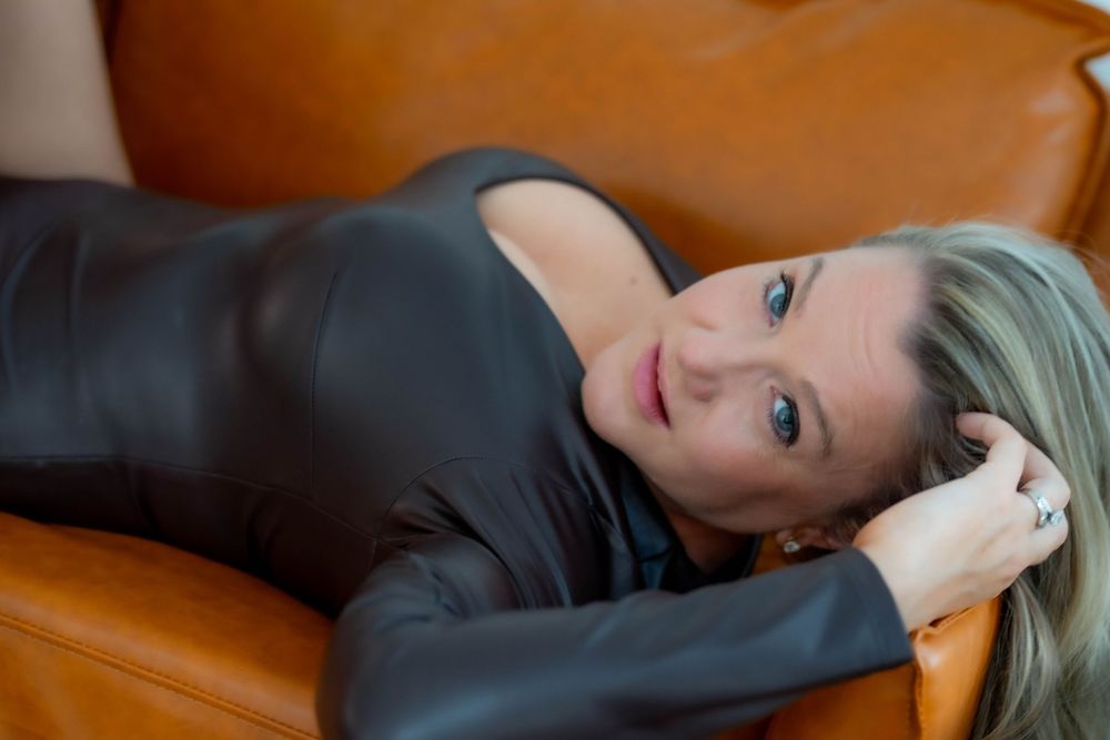 Person relaxing on brown leather couch in dimly lit room.