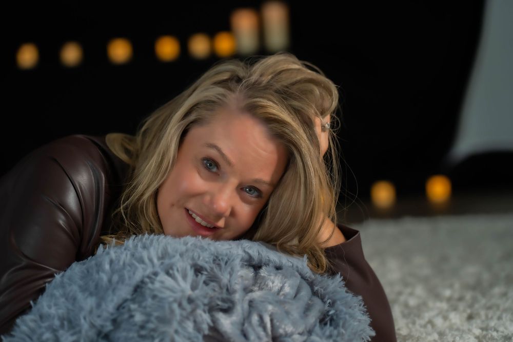 Person posing with grey fluffy pillow in dark room with ambient lighting.
