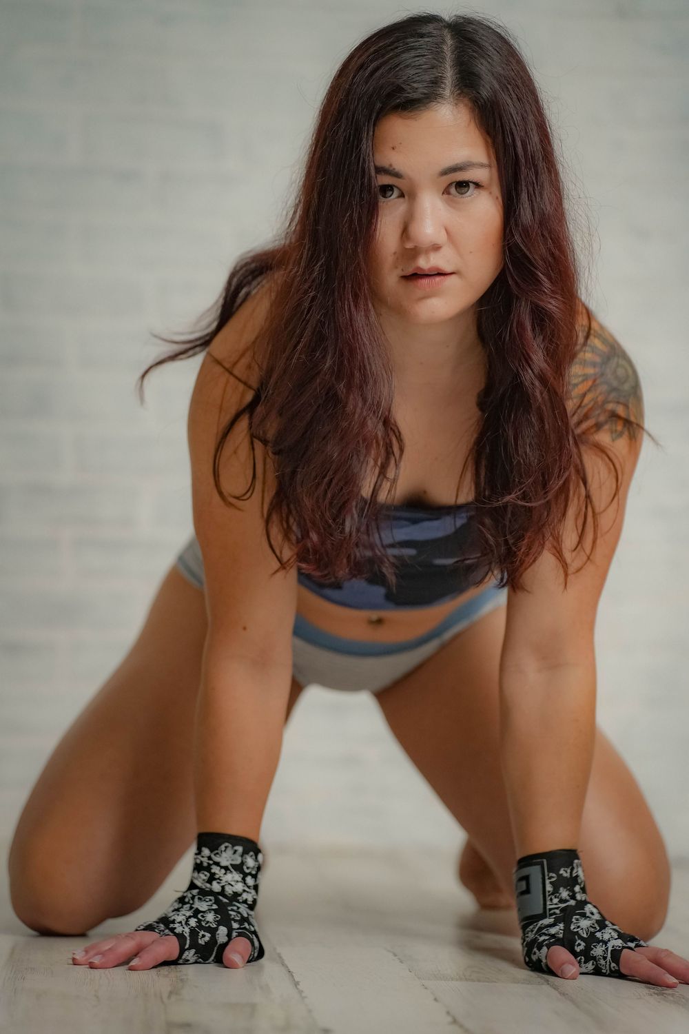 A female MMA fighter in workout attire and fingerless gloves poses in a crouched position on a gym floor.