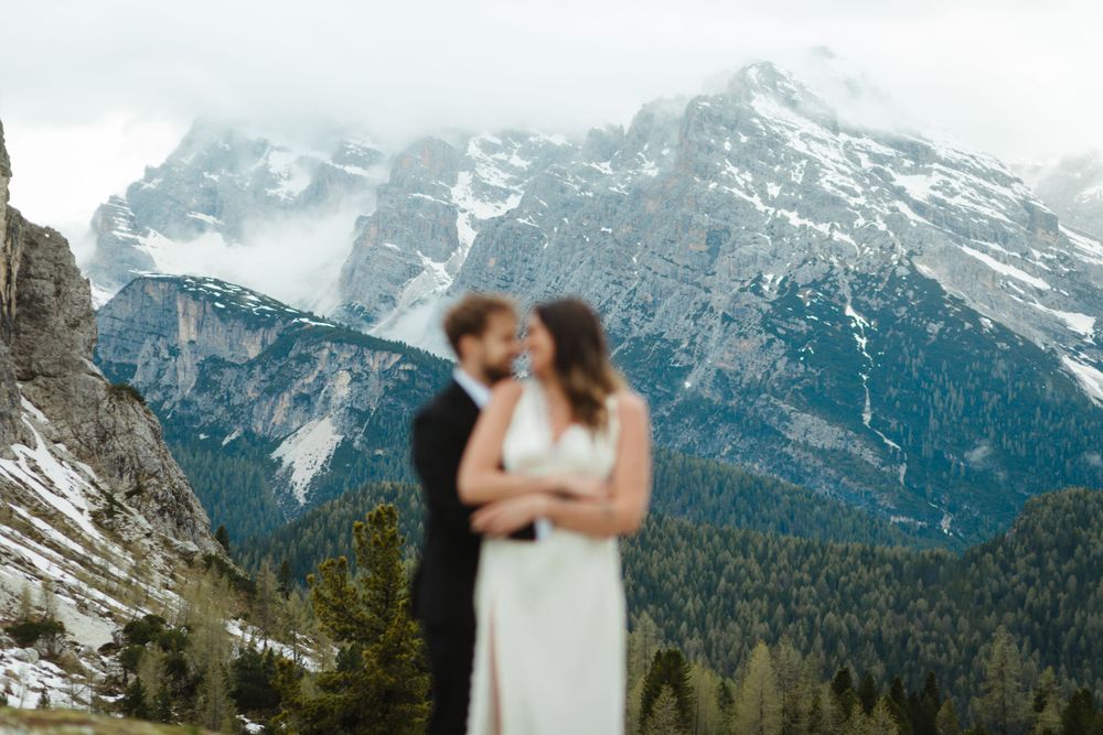 A romantic embrace with majestic mountain peaks and evergreen forest creating a stunning backdrop.