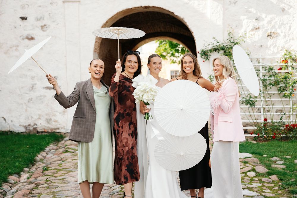 Wedding party in white and floral dresses pose together in garden setting.