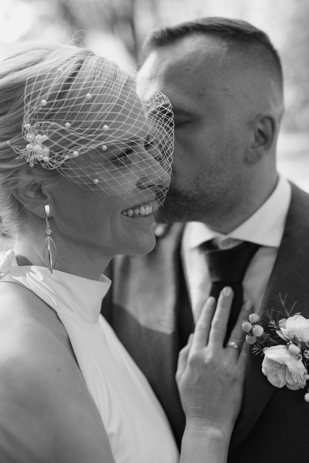Black and white wedding photo showing tender moment with bride in vintage birdcage veil.