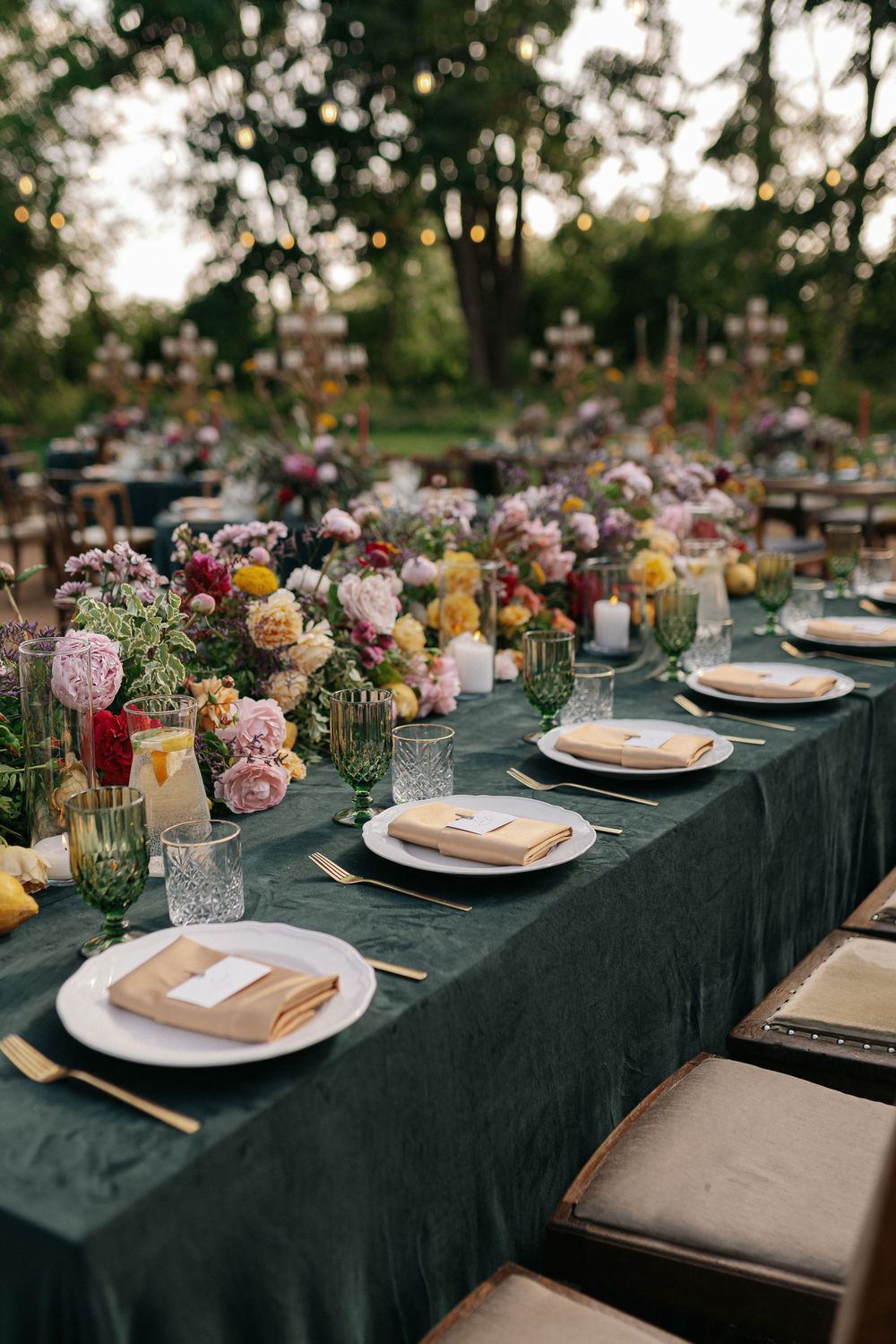 Elegant wedding table setting with dark tablecloth and colorful floral centerpieces outdoors.