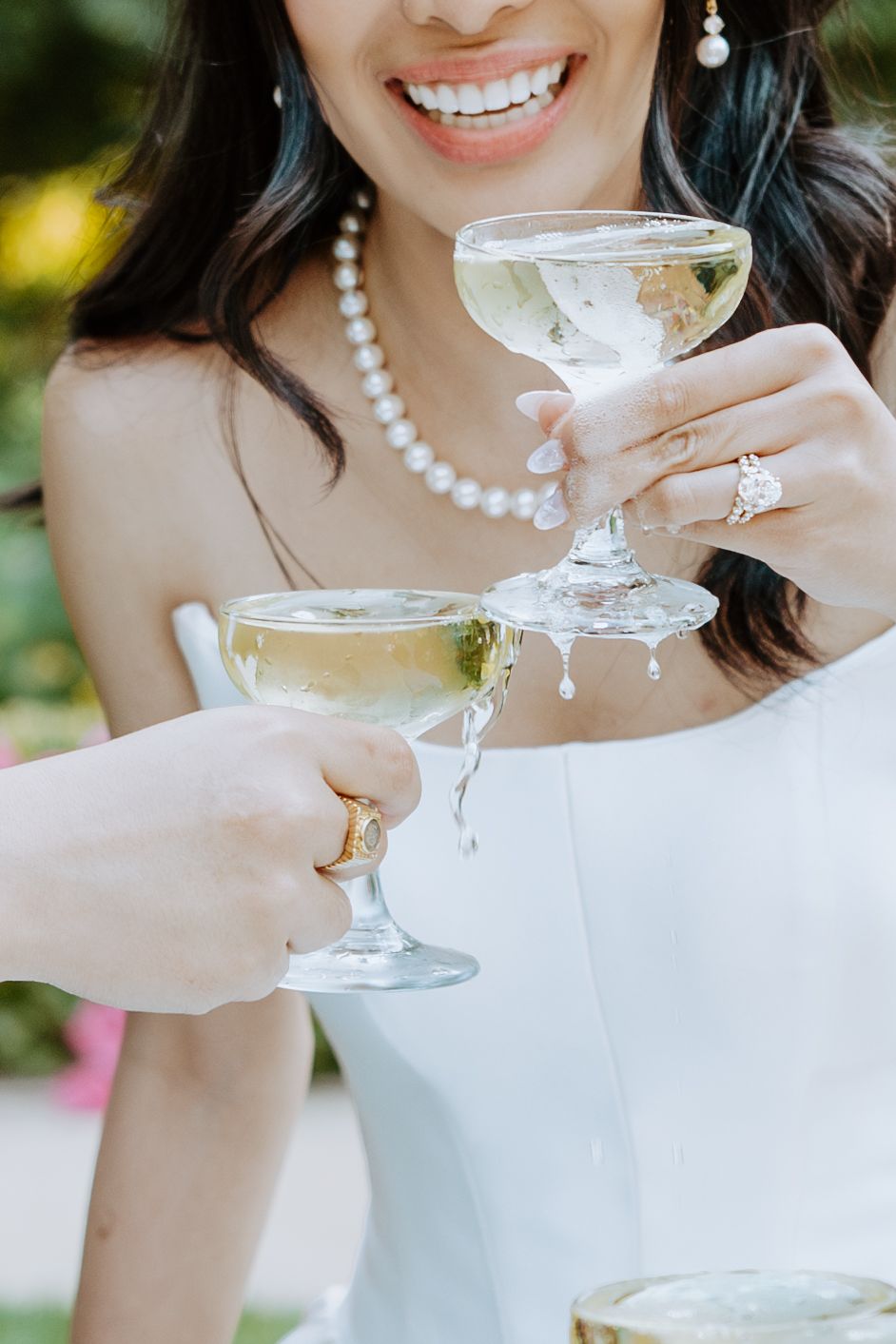 Wedding party toasting with champagne glasses while wearing elegant pearl necklaces and formal attire.