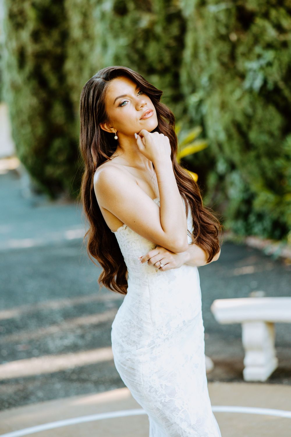 Elegant white lace wedding dress shown in outdoor garden setting with soft natural lighting and greenery backdrop.