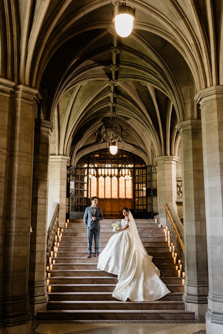 Bride and groom pose on grand staircase beneath arches during elegant Knox College wedding.
