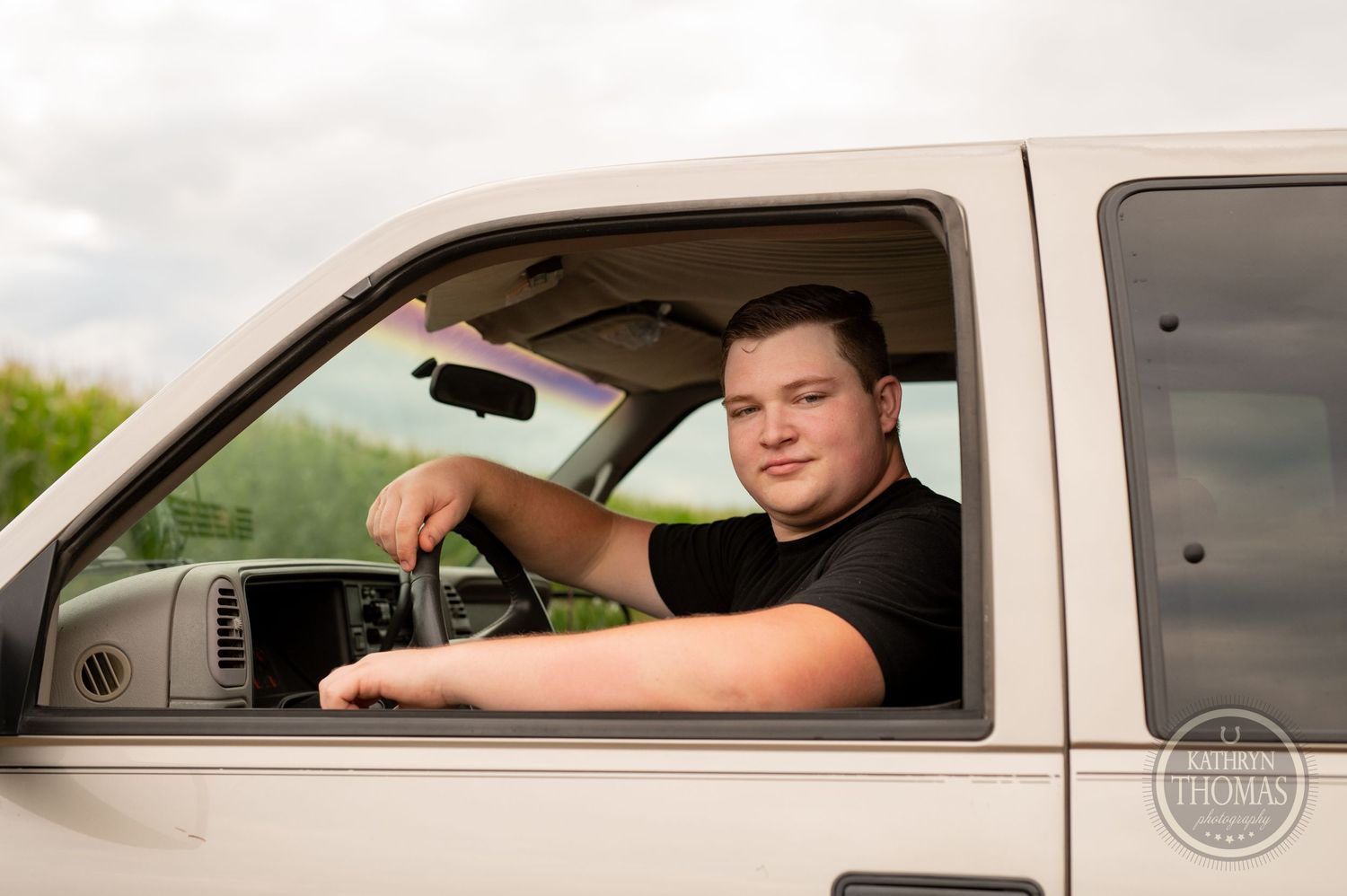 A person sits in the driver's seat of a light-colored Chevrolet pickup truck.
