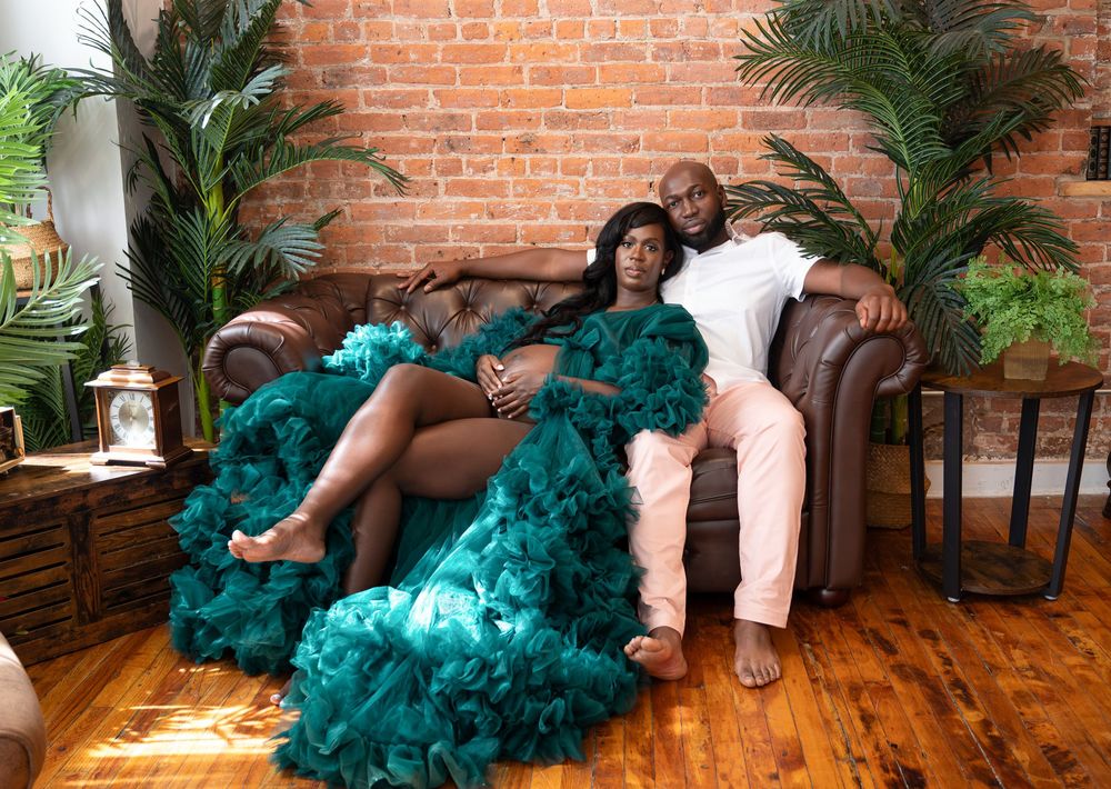 A couple lounges on a leather sofa against an exposed brick wall with tropical plants in a bohemian-styled setting.
