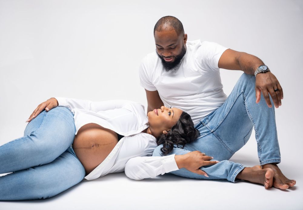 A couple in casual denim and white outfits pose intimately together during a relaxed studio photo session.