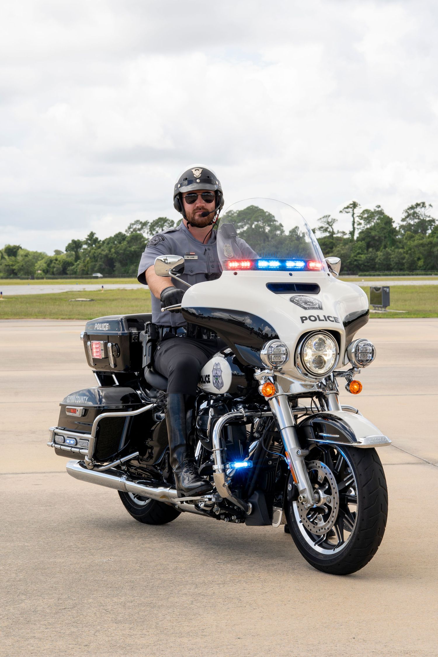 Three white police motorcycles parked on asphalt with emergency lights and official law enforcement markings visible.