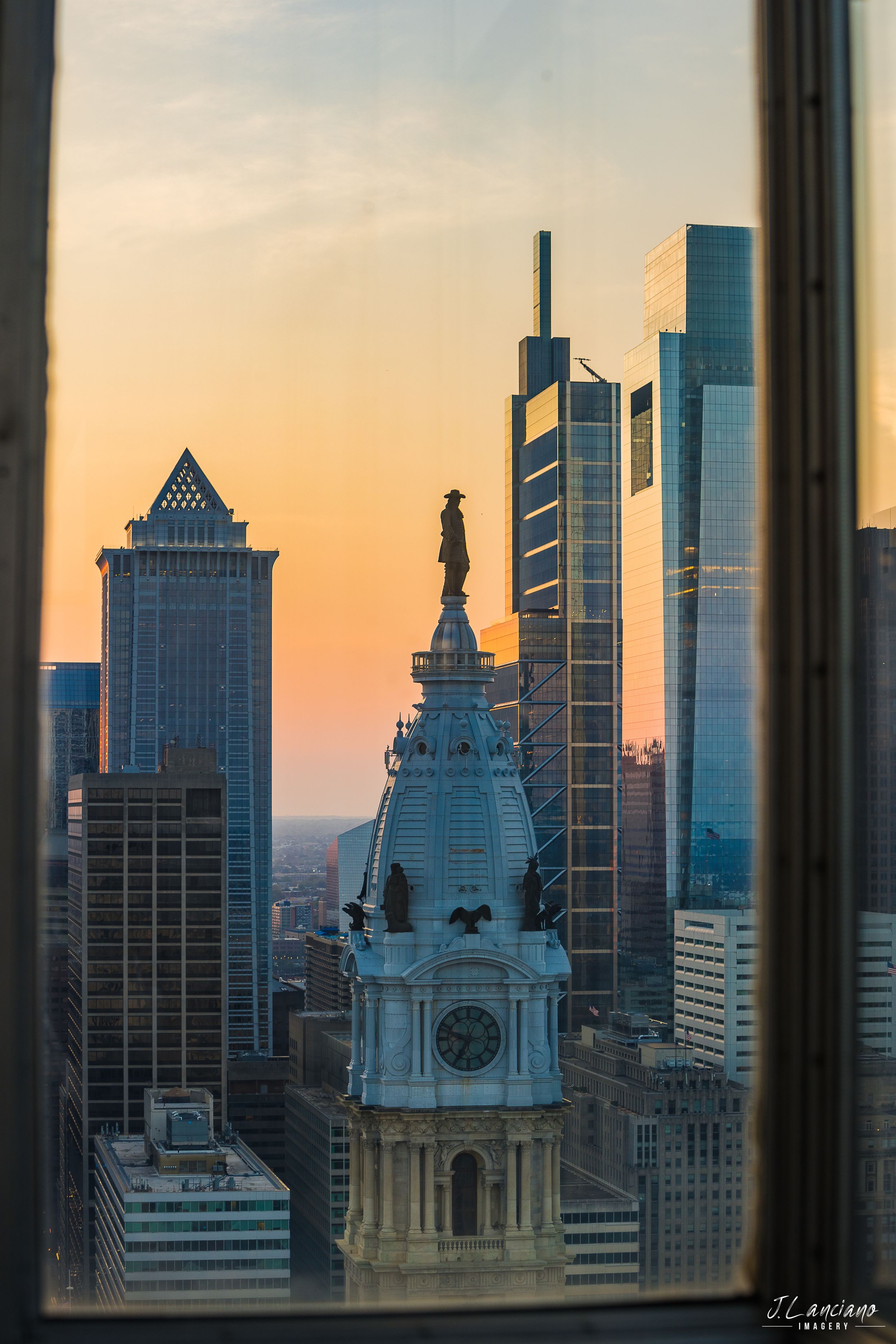 Philadelphia City Hall and modern skyscrapers during sunset viewed through window.
