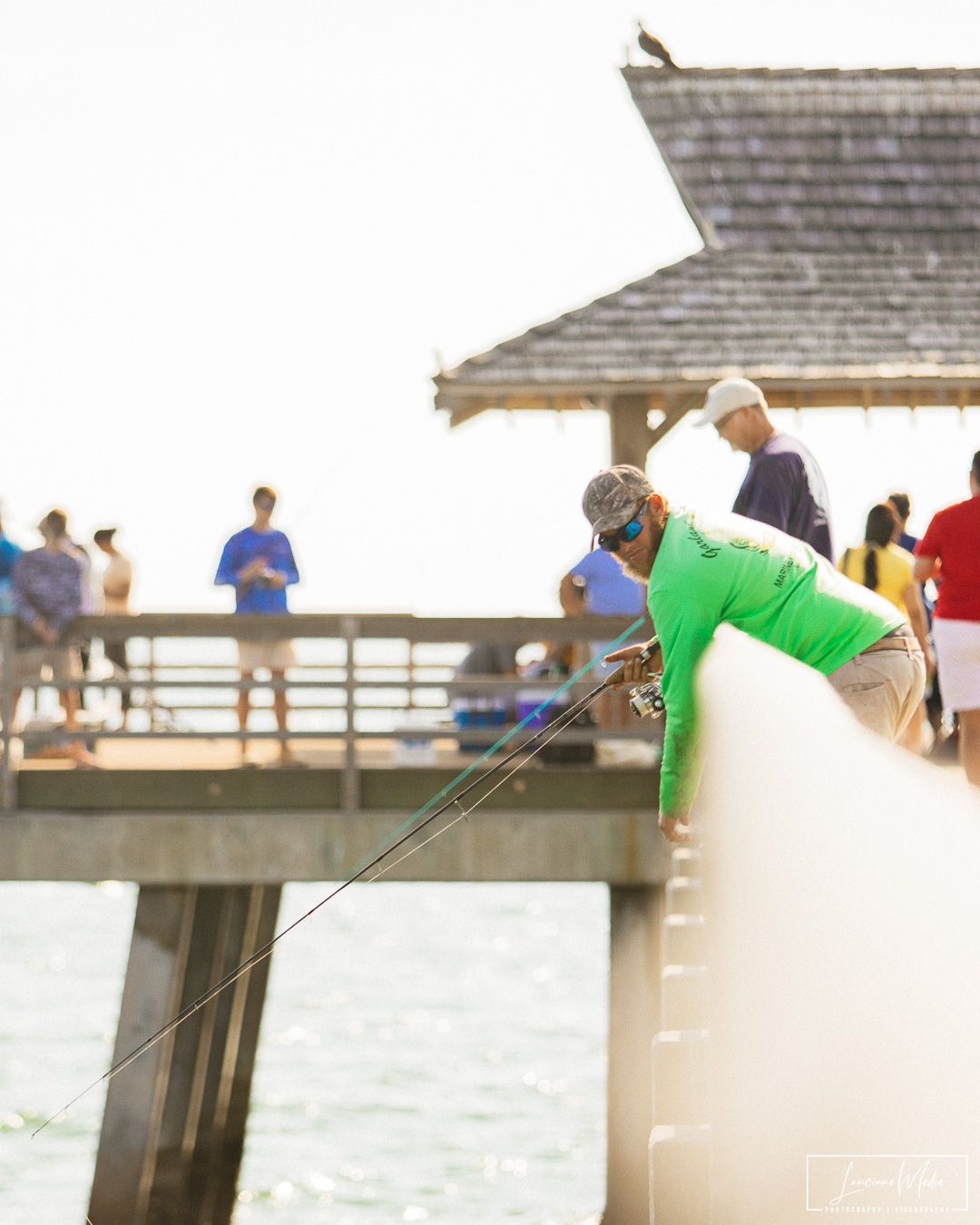 People fishing from wooden pier during sunset at beach.