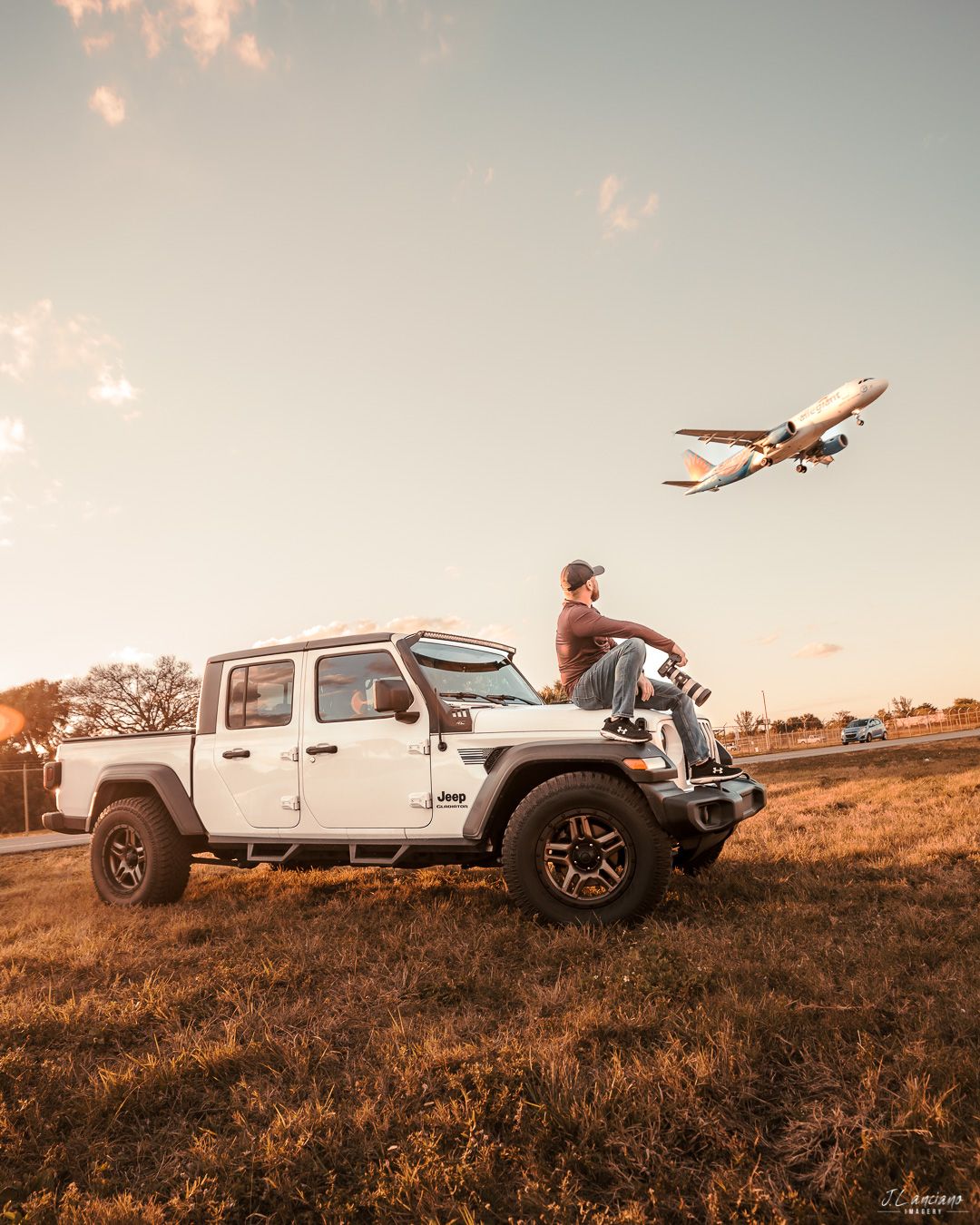 Jeep parked on hilltop at sunset with commercial airplane flying overhead.