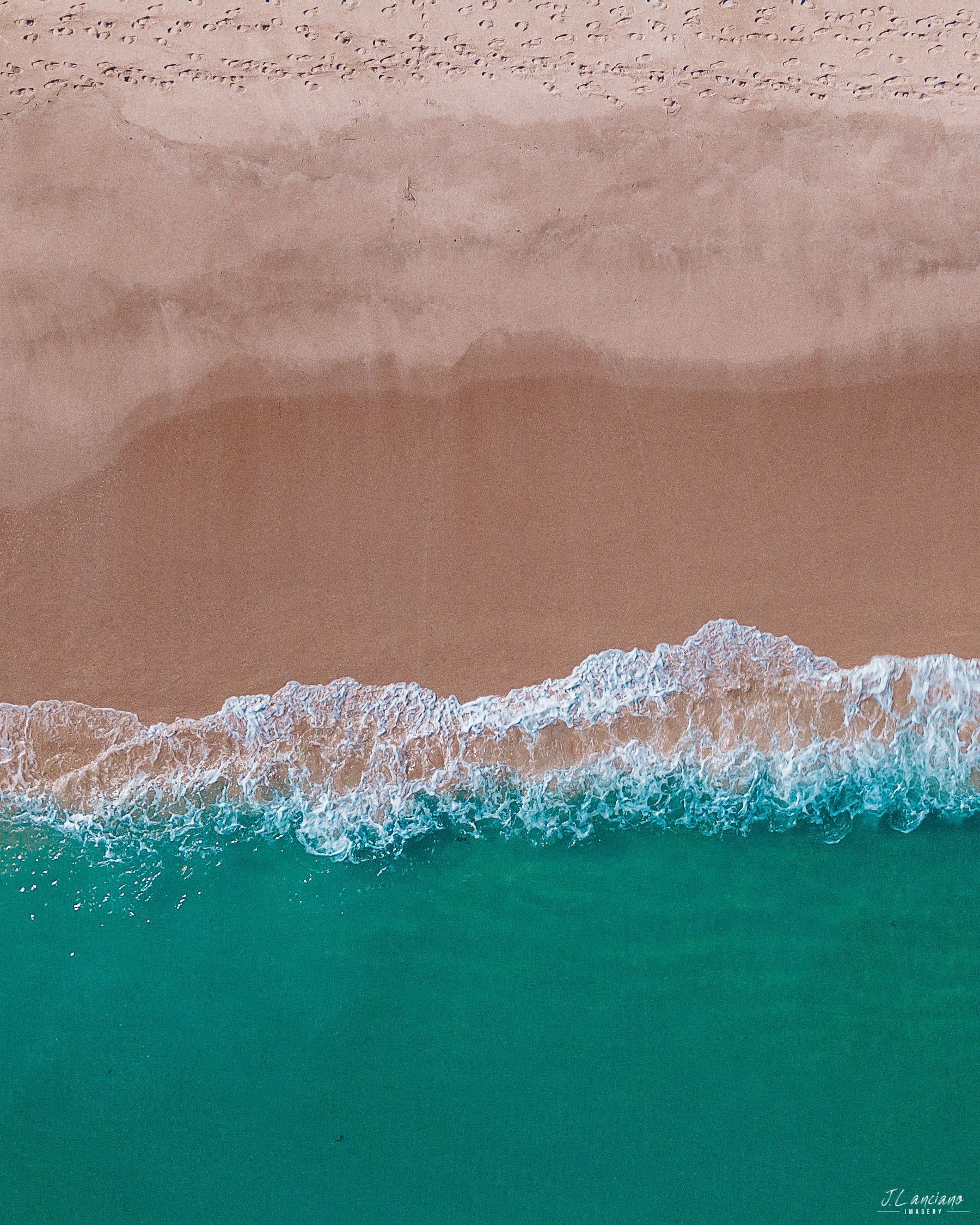 Aerial view of turquoise ocean waves meeting pink sandy beach creating a stunning contrast.