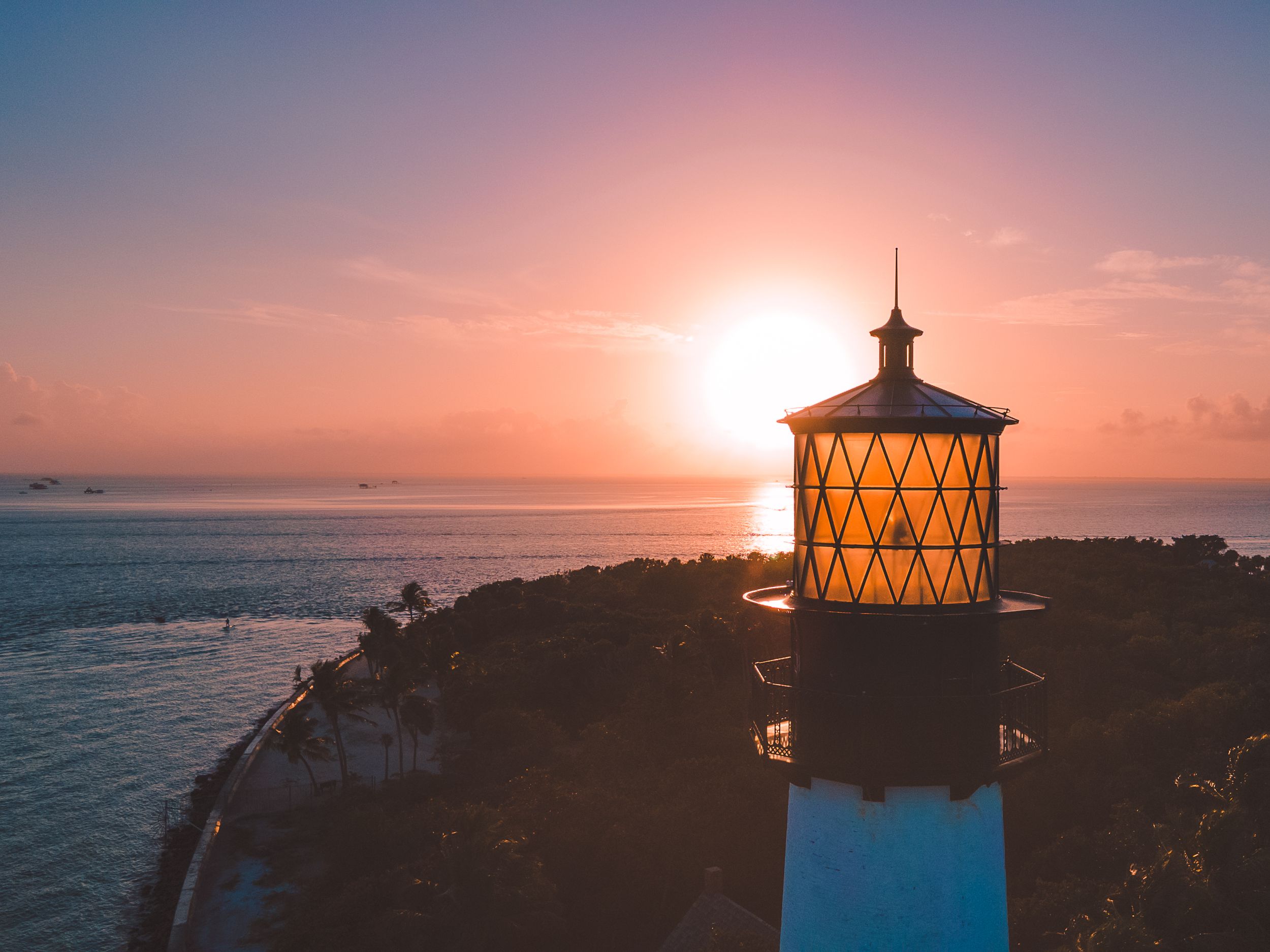 Glowing lighthouse tower silhouetted against a vibrant orange sunset over the ocean.