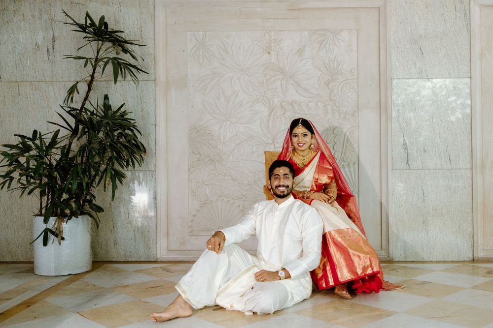 Couple in traditional Indian wedding attire posing in elegant marble interior with potted plant.