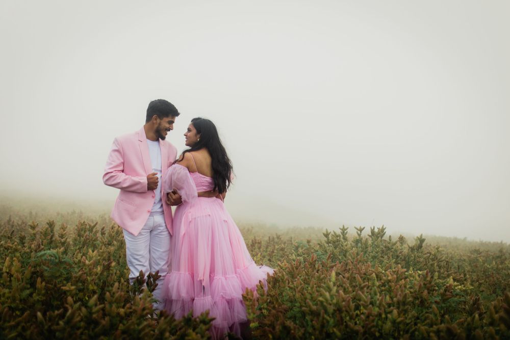 Couple in pink outfits embracing in misty field of wildflowers.