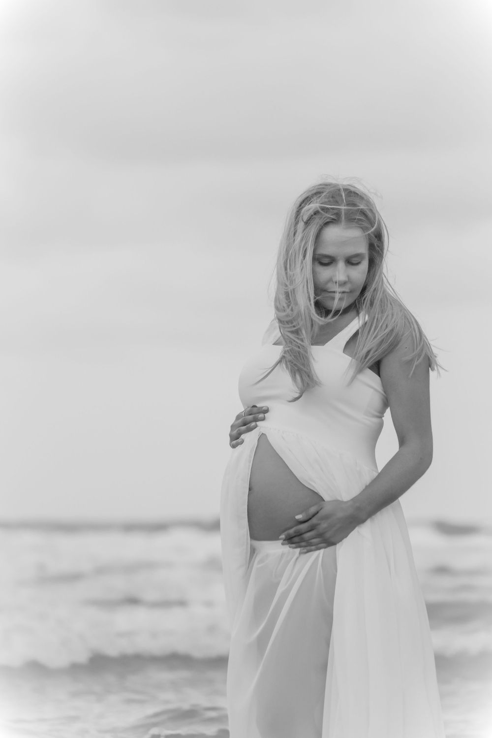 A black and white maternity photo of an expectant mother by the ocean.