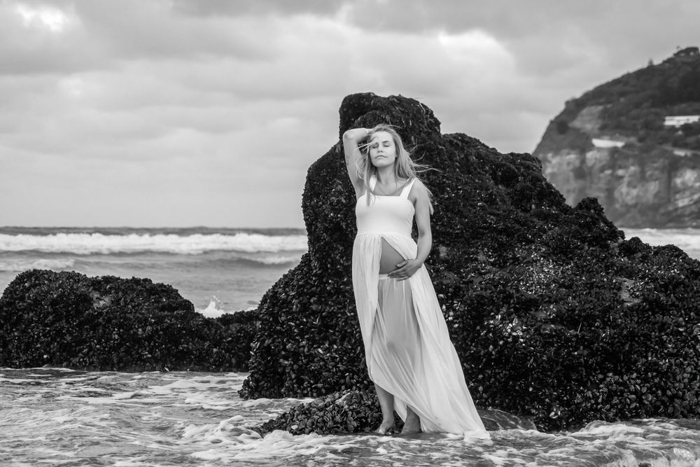 A black and white beach portrait with dramatic rocky coastal formations in the background.