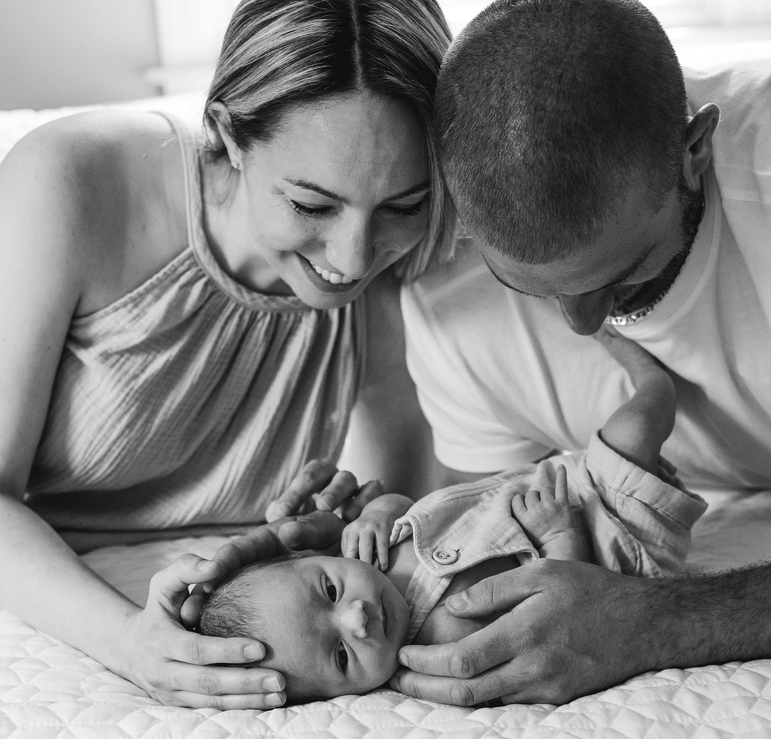 Intimate black and white portrait of new parents with their baby on bed.