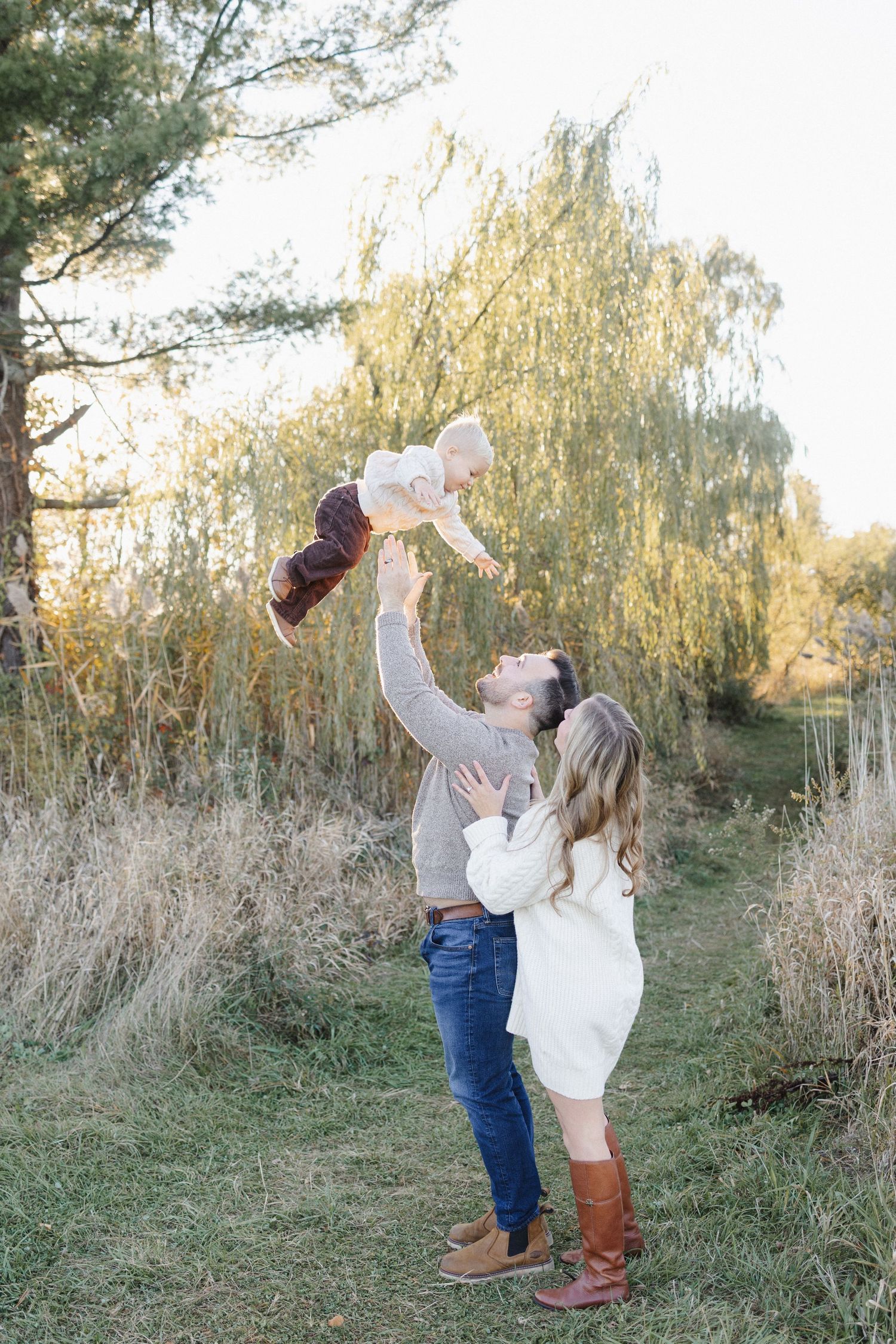 Family shares joyful laughter while playing and holding child upside down in garden setting.