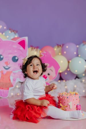 Cake smash photo session with pink cat decorations and festive balloon background.