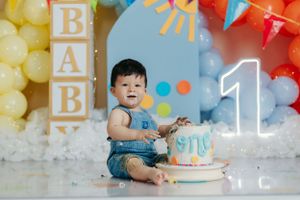 First birthday celebration with blue and yellow balloons, blocks spelling BAB, and small cake.