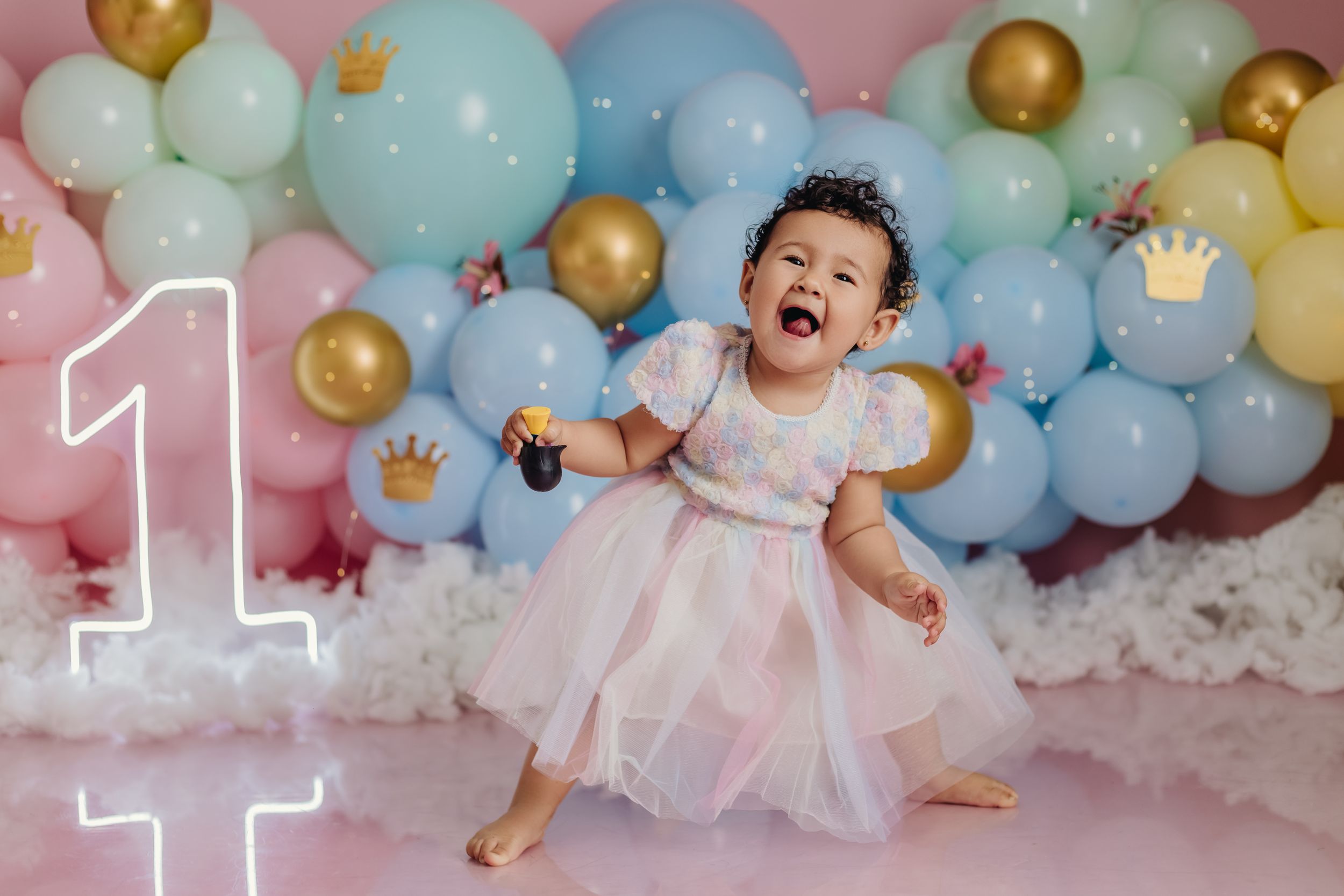 First birthday celebration with pastel balloon arch and gold accents.