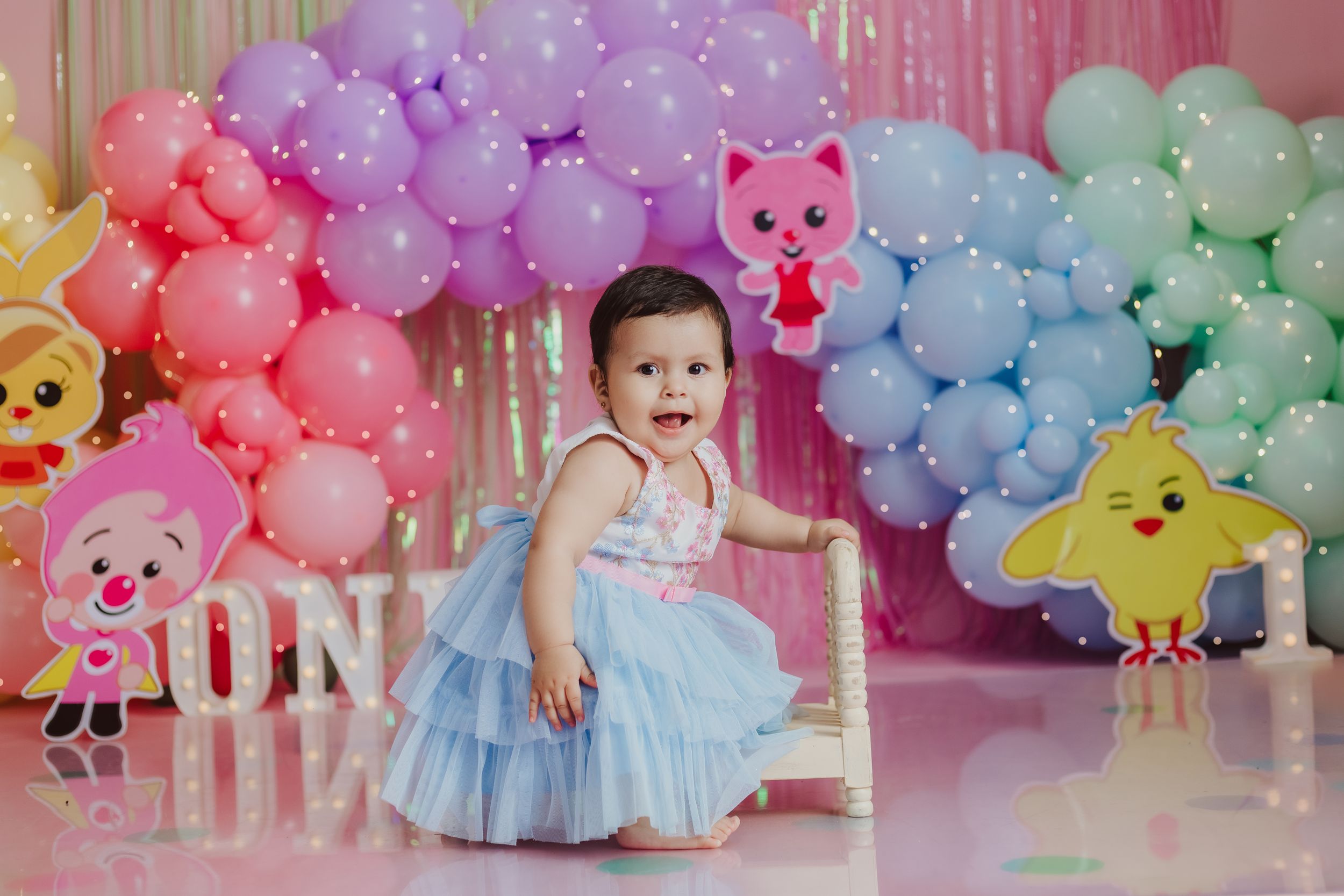 Colorful rainbow balloon arch with cartoon animal decorations at a birthday party.