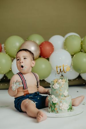 Cake smash photography session with mint green balloon backdrop and tiered birthday cake.