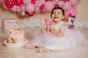 Pink themed first birthday celebration with balloon arch and delicate cake setup.