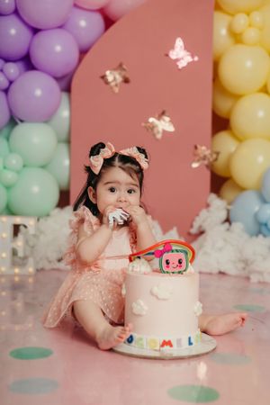 Pink and pastel balloon backdrop with butterfly decorations and white birthday cake.