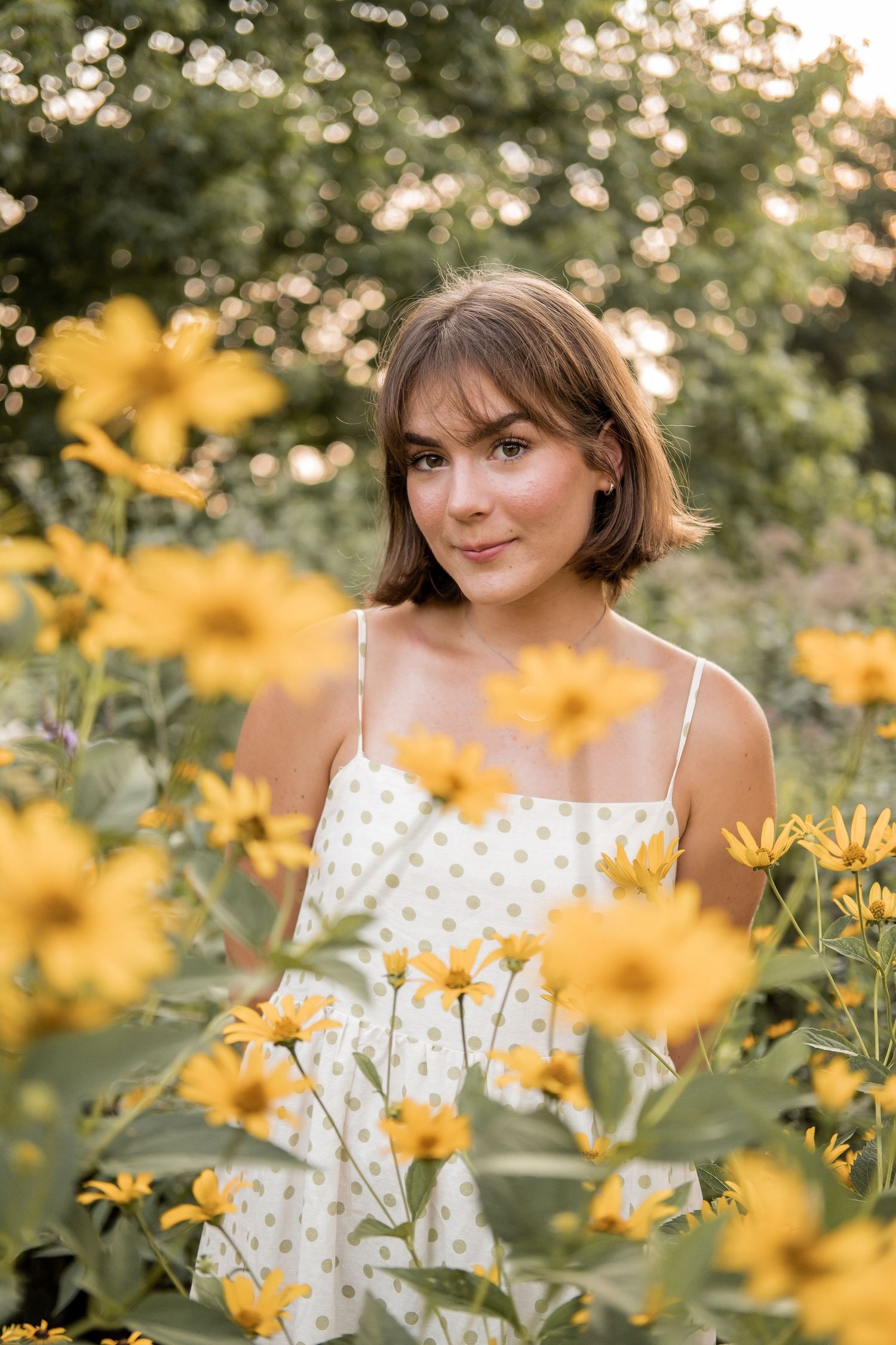 A white polka dot sundress stands out among vibrant yellow flowers in a summer garden setting.