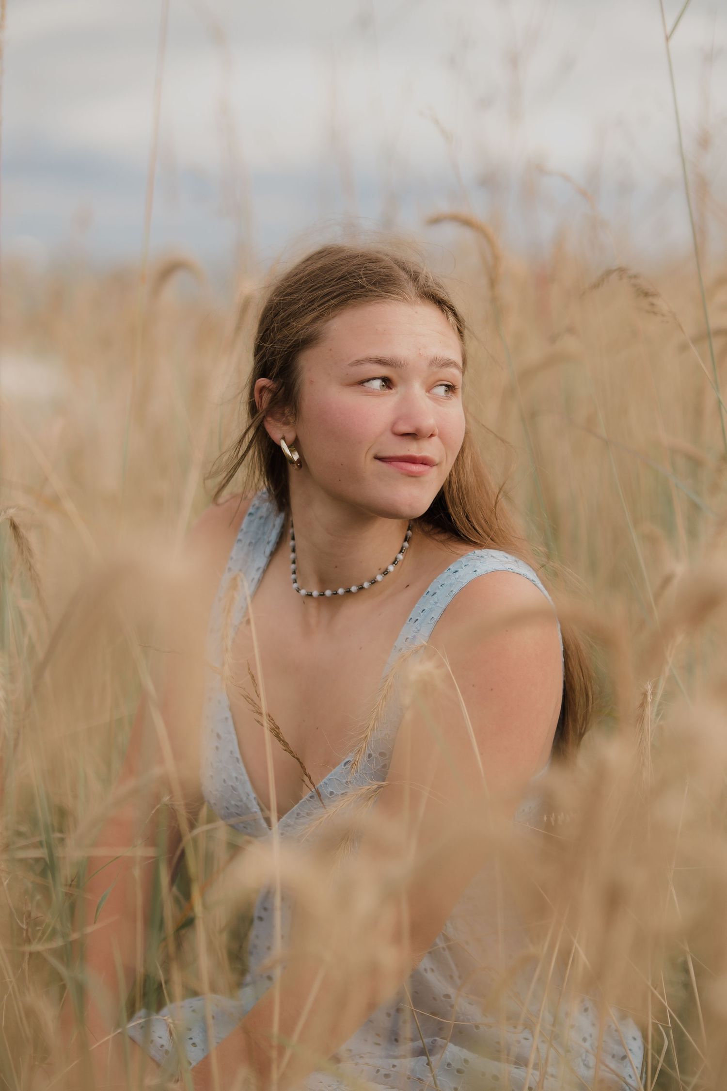 Person in blue top posing among tall wheat grass during golden hour.