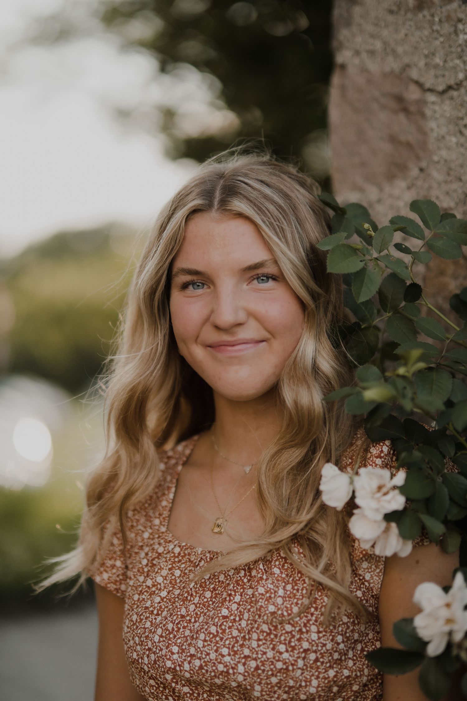 Person in sparkly brown dress poses near white flowers in natural outdoor setting.
