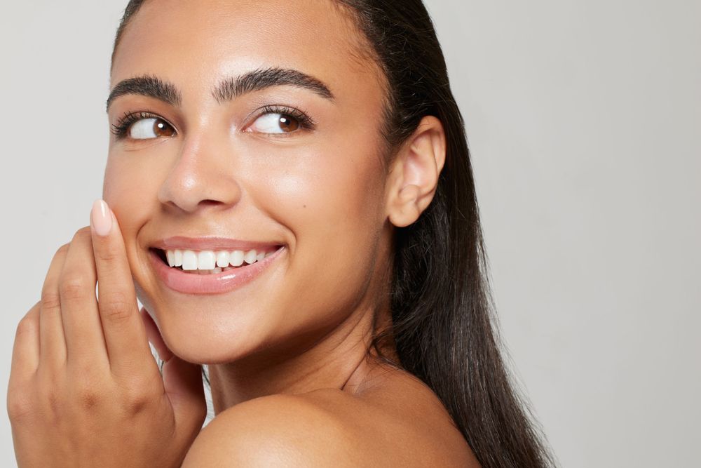 Beauty portrait showcasing glowing skin and natural makeup against neutral background.