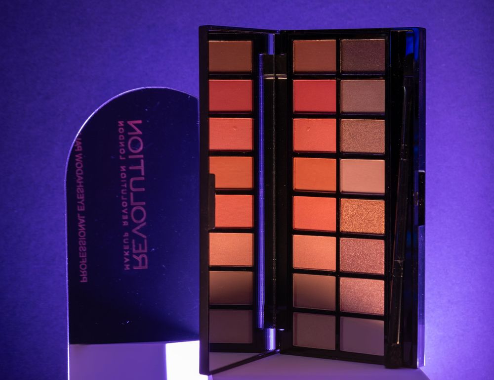 Makeup palette with orange and brown shades against a purple background.