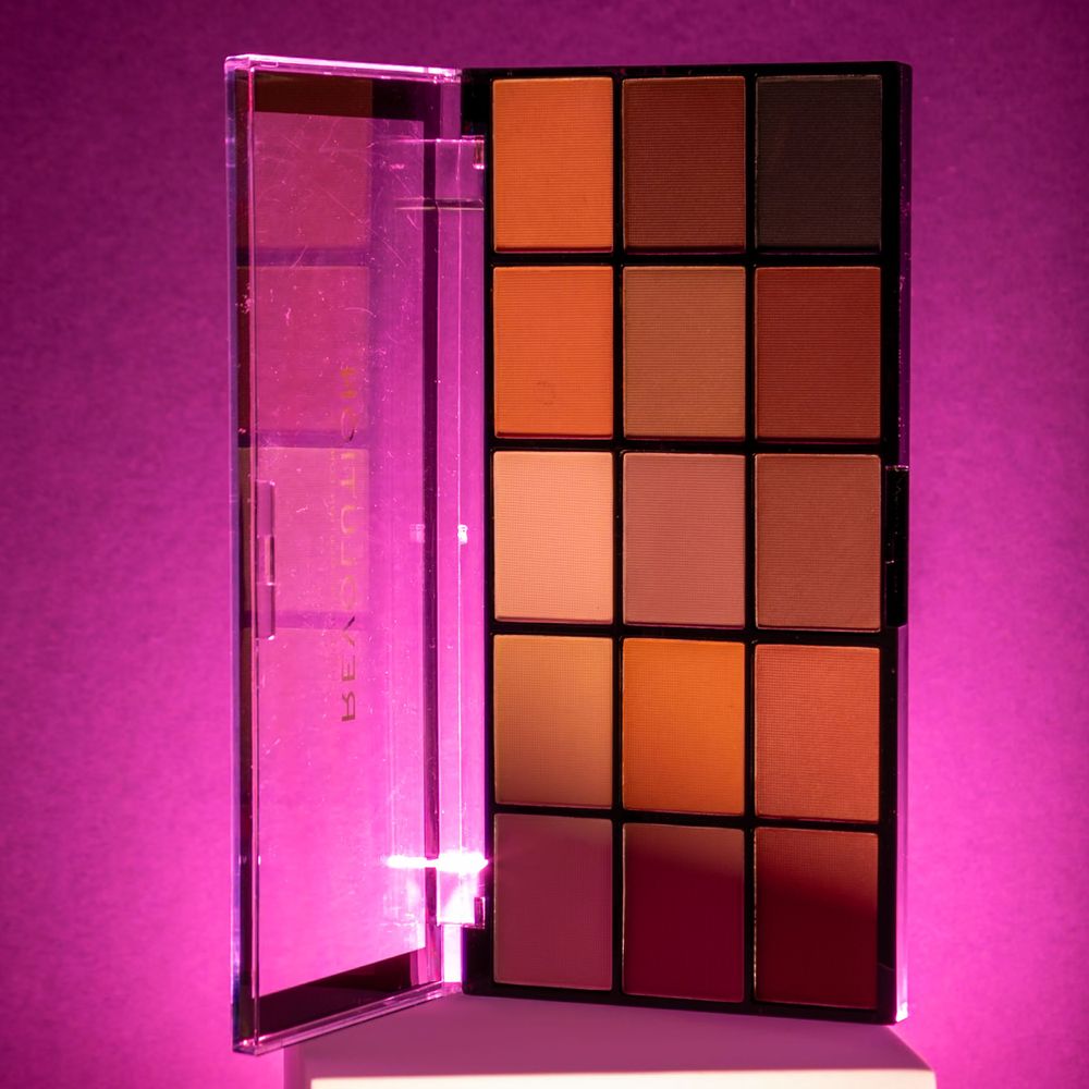 Eyeshadow palette with warm tones displayed against a pink gradient background.