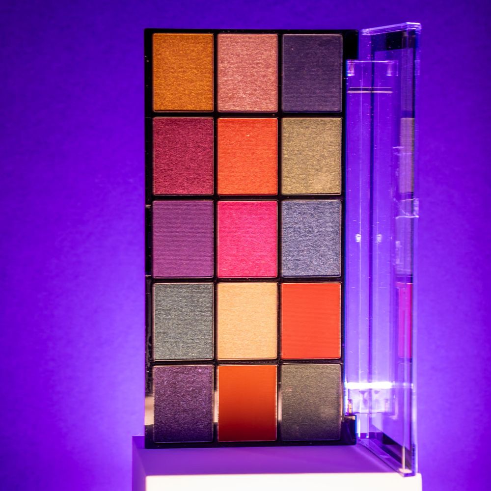 Makeup palette with orange and metallic shades photographed against purple lighting.
