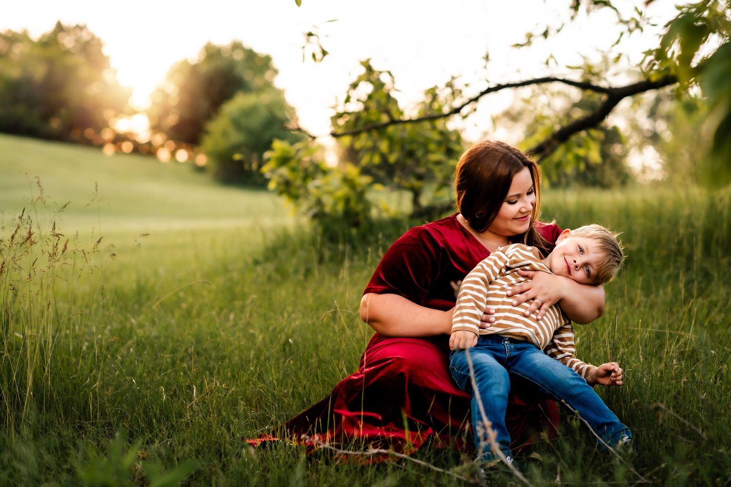 Parent and child sharing tender moment in sunlit field at sunset.