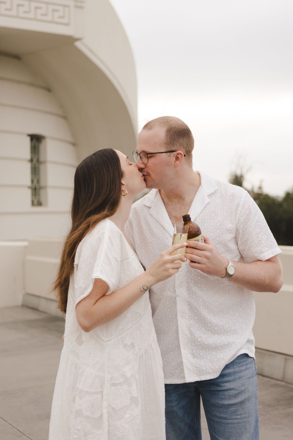 Romantic moment shared in white outfits against architectural backdrop.