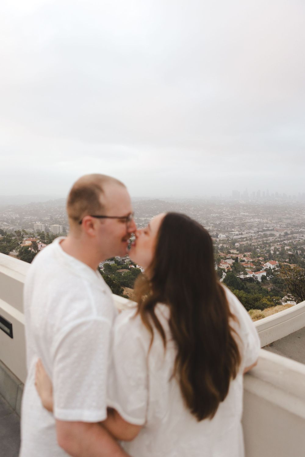 A tender moment shared at the Griffith Observatory overlook with LA cityscape in background.