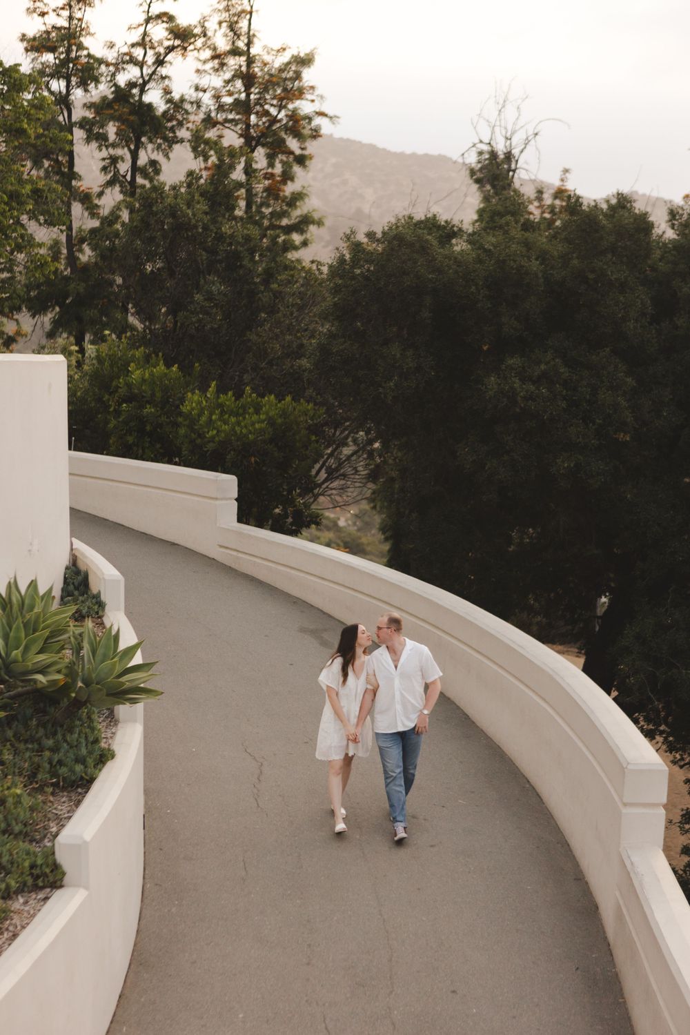 A couple strolls along the curved walkway at Griffith Observatory with city views below.